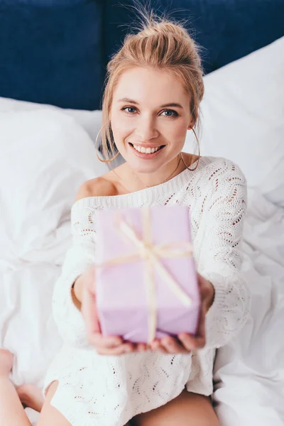 Selective focus of attractive happy woman holding gift on bed — Stock Photo