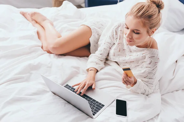 Приваблива жінка купує онлайн з ноутбуком і кредитною карткою на ліжку вранці — стокове фото