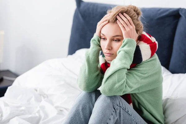 Mujer enferma en suéter y bufanda con dolor de cabeza sentado en la cama - foto de stock