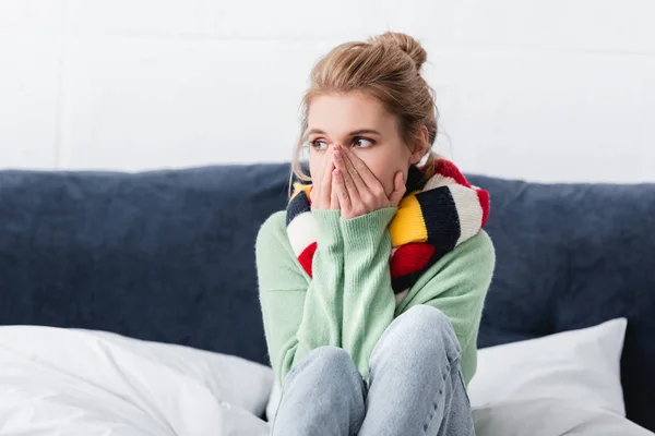 Mujer joven enferma en suéter y bufanda sentada en la cama - foto de stock