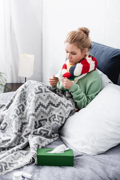 Bouleversé femme malade dans l'écharpe tenant des pilules dans le lit avec des serviettes — Photo de stock