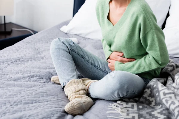 Обрізаний вид жінки з болем в животі і сидить на ліжку — Stock Photo
