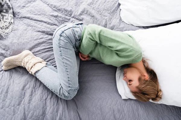 Vista superior de la mujer con dolor abdominal y acostada en la cama - foto de stock