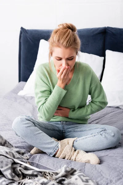 Jeune femme ayant des nausées et assise sur le lit avec tablette numérique — Photo de stock