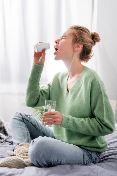 Frau mit Schmerzen nimmt Tabletten und hält Glas Wasser im Schlafzimmer — Stockfoto