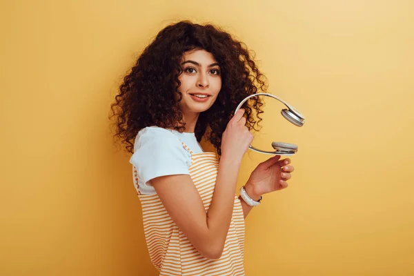 Smiling mixed race girl looking away while holding wireless headphones on yellow background — Stock Photo
