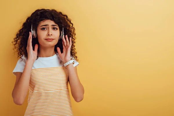 Verärgertes zweirassiges Mädchen, das Musik in Kopfhörern auf gelbem Hintergrund hört — Stockfoto