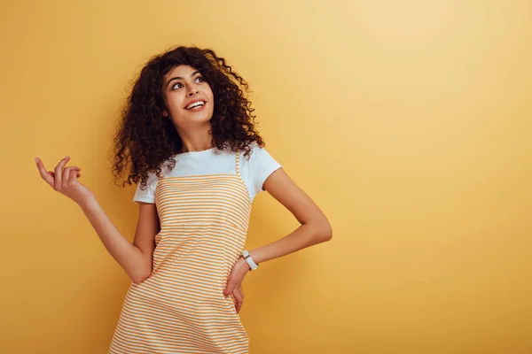 Щаслива бі-расова дівчина дивиться геть, стоячи з рукою на стегні на жовтому тлі — стокове фото
