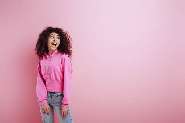 Glückliches zweirassiges Mädchen lacht, während es auf rosa Hintergrund wegschaut — Stock Photo