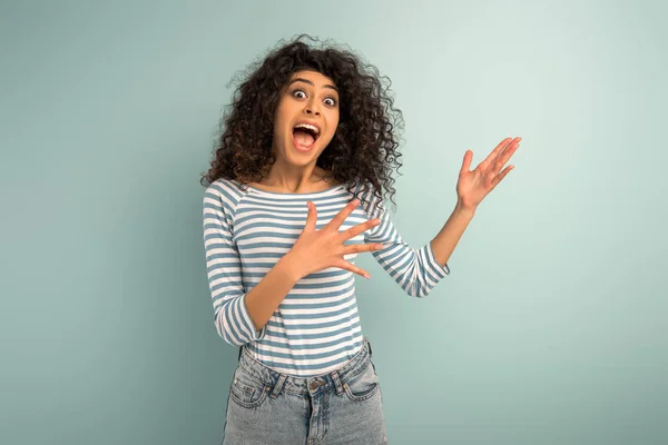 Shocked mixed race girl pointing with hands while looking at camera on grey background — Stock Photo