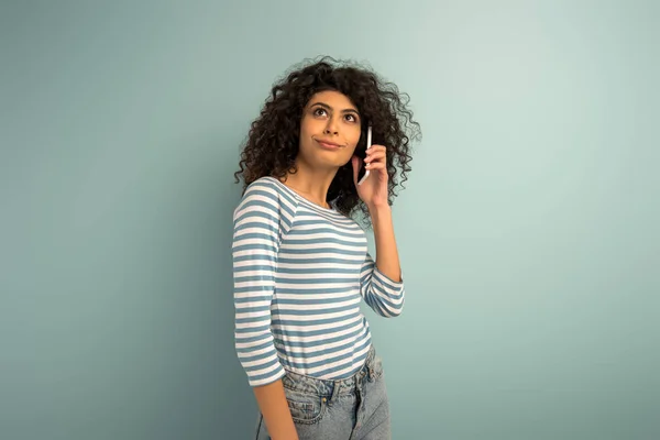 Skeptical mixed race looking away while talking on smartphone on grey background — Stock Photo