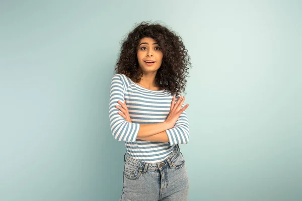 Skeptical mixed race girl looking at camera while standing with crossed arms on grey background — Stock Photo