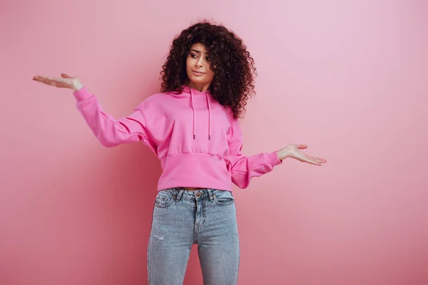 Atractiva chica bi-racial de pie con los brazos abiertos y sonriendo sobre fondo rosa - foto de stock