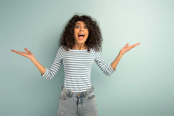 Excité mixte race fille regardant caméra tandis que debout avec les bras ouverts sur fond gris — Photo de stock