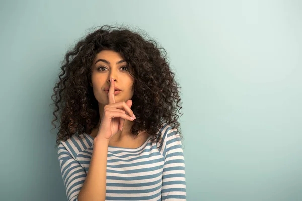 Pretty mixed race girl showing hush gesture while looking at camera on grey background — Stock Photo