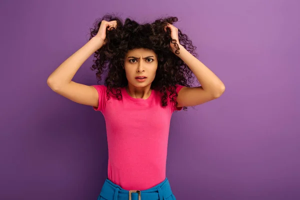 Wütendes bi-rassisches Mädchen, das Haare berührt, während es in die Kamera auf lila Hintergrund schaut — Stockfoto