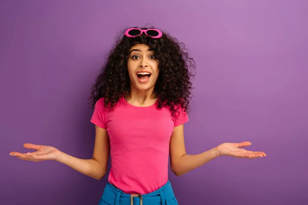 Deluso bi-razziale ragazza mostrando gesto scrollata di spalle mentre guardando la fotocamera su sfondo viola — Foto stock