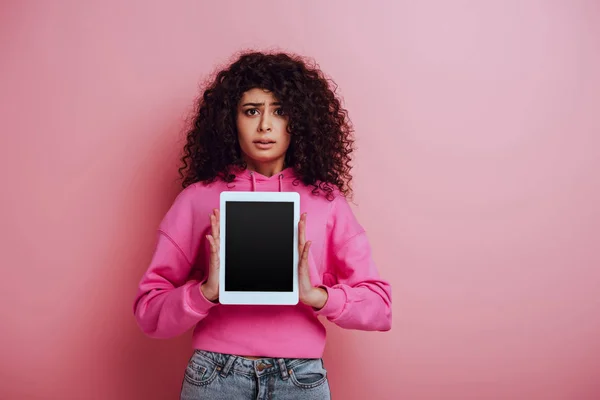 Enttäuschtes zweirassiges Mädchen, das in die Kamera schaut, während es ein digitales Tablet mit leerem Bildschirm auf rosa Hintergrund zeigt — Stockfoto