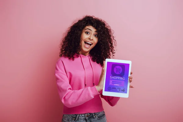 Excitée fille bi-raciale montrant tablette numérique avec application shopping sur fond rose — Photo de stock