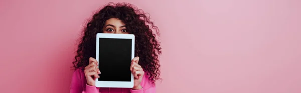 Panoramaaufnahme eines zweirassigen Mädchens, das ein digitales Tablet mit leerem Bildschirm auf rosa Hintergrund zeigt — Stockfoto
