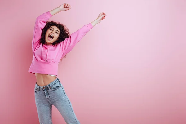 Glückliches zweirassiges Mädchen, das mit erhobenen Händen auf rosa Hintergrund in die Kamera blickt — Stockfoto
