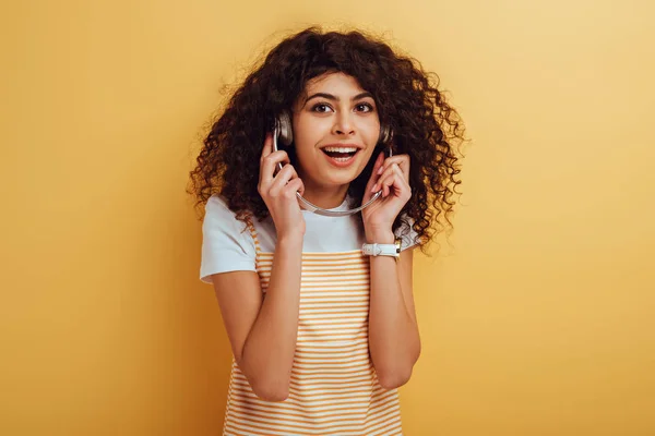 Lächelndes Mischlingsmädchen, das wegschaut, während es Musik in Kopfhörern auf gelbem Hintergrund hört — Stockfoto