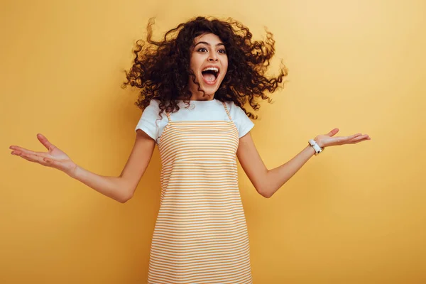 Excited mixed race girl looking away while standing with open mouth on yellow background — Stock Photo