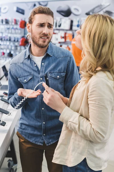 Sad boyfriend talking with girlfriend with smartphone in home appliance store — Stock Photo