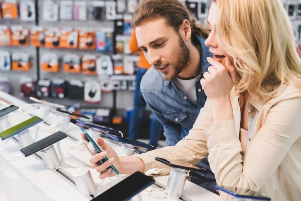 Novio y novia sorprendida mirando nuevo teléfono inteligente en la tienda de electrodomésticos - foto de stock