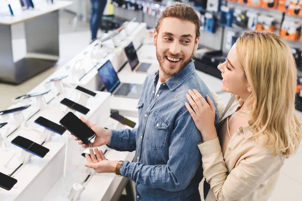 Sorrindo namorado segurando novo smartphone e falando com a namorada na loja de eletrodomésticos — Fotografia de Stock