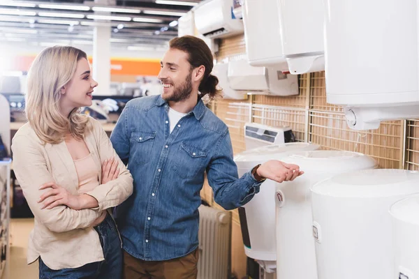 Smiling boyfriend and girlfriend talking near boilers in home appliance store — Stock Photo
