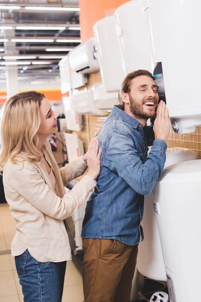 Lächelnder Freund berührt Heizkessel und Freundin schaut ihn im Haushaltsgerätegeschäft an — Stockfoto