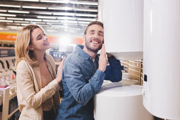 Lächelnder Freund berührt Heizkessel und Freundin schaut ihn im Haushaltsgerätegeschäft an — Stockfoto