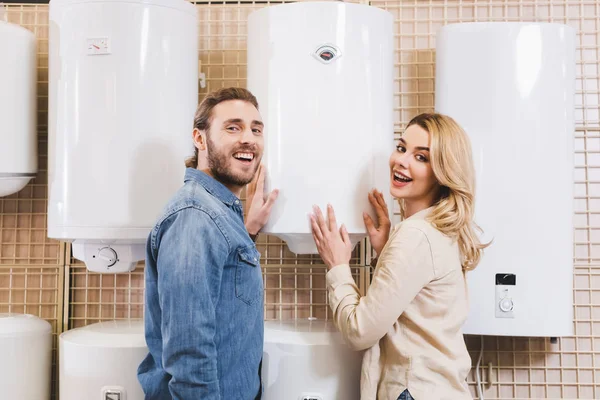 Smiling boyfriend and girlfriend touching boiler in home appliance store — Stock Photo