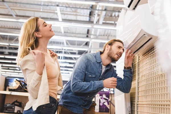 Petit ami regardant climatiseur et souriant petite amie refroidissement dans le magasin d'appareils ménagers — Photo de stock