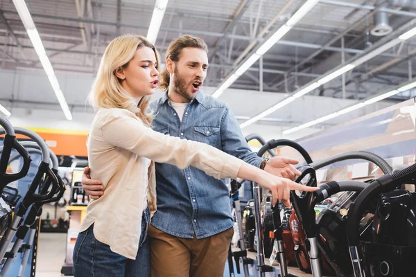 Sorprendido novio y novia apuntando con el dedo a la nueva aspiradora en la tienda de electrodomésticos - foto de stock