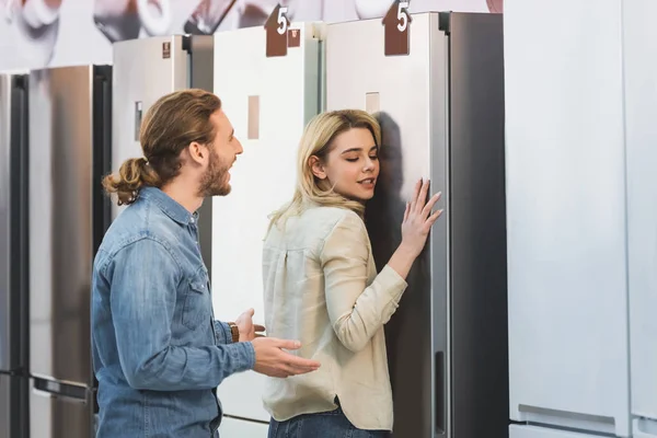 Girlfriend touching fridge and shocked boyfriend looking at her in home appliance store — Stock Photo