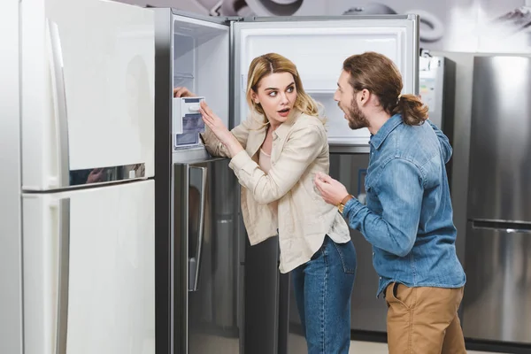 Shocked boyfriend and girlfriend standing near fridge in home appliance store — Stock Photo