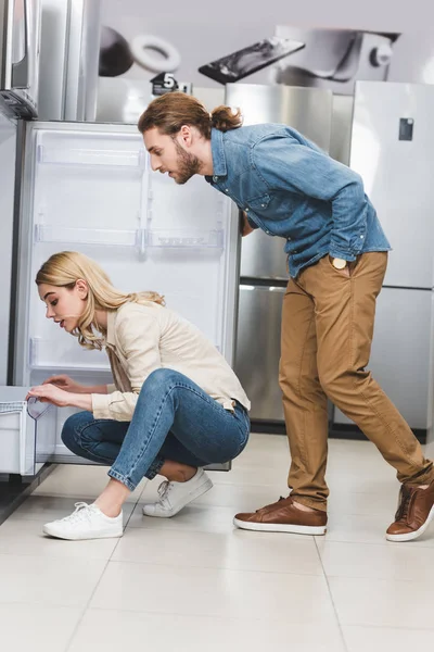 Side view of boyfriend and girlfriend looking at fridge in home appliance store — Stock Photo