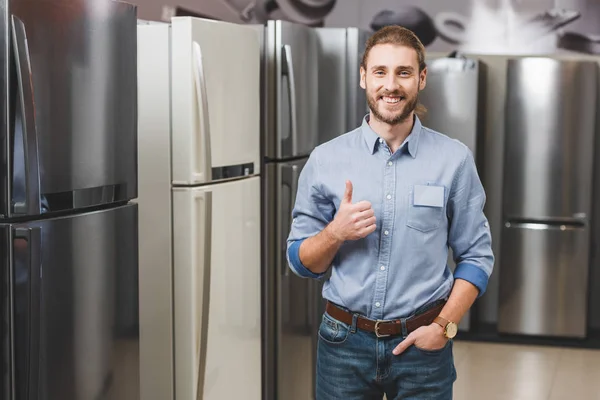 Consultor sorrindo mostrando como perto de frigoríficos na loja de eletrodomésticos — Fotografia de Stock