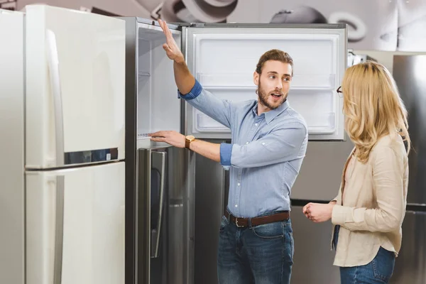 Berater spricht mit Frau und zeigt Kühlschrank im Haushaltsgerätehaus — Stockfoto