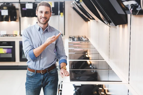 Consultant souriant pointant avec la main sur les hottes de cuisinière dans le magasin d'appareils ménagers — Photo de stock