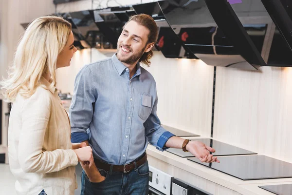 Consultor sonriente hablando con la mujer cerca de campanas de cocina y cocinas en la tienda de electrodomésticos - foto de stock