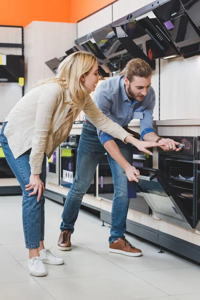 Consultor uso horno y mujer sonriente señalando con la mano en la tienda de electrodomésticos - foto de stock