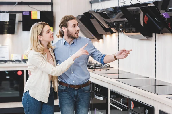 Consultant choqué et souriante femme pointant avec les doigts à la hotte de la cuisinière dans le magasin d'appareils ménagers — Photo de stock