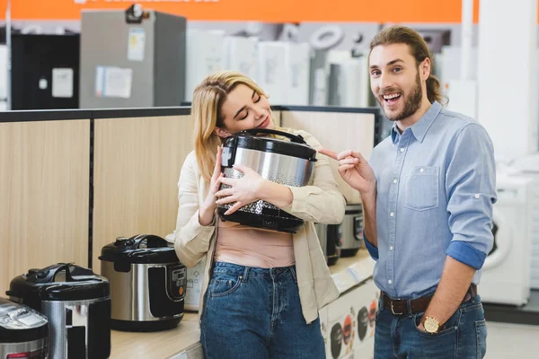 Consultant souriant pointant du doigt la femme avec cuisinière lente dans le magasin d'appareils ménagers — Photo de stock