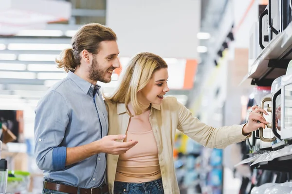 Consulente sorridente e donna guardando il forno a microonde nel negozio di elettrodomestici — Foto stock