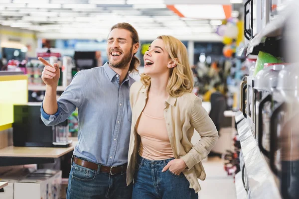 Consulente che punta con dito e donna sorridente in piedi vicino a microonde nel negozio di elettrodomestici — Foto stock