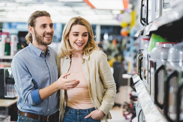 Consultant souriant pointant du doigt au micro-ondes et parlant avec la femme dans le magasin d'appareils ménagers — Photo de stock