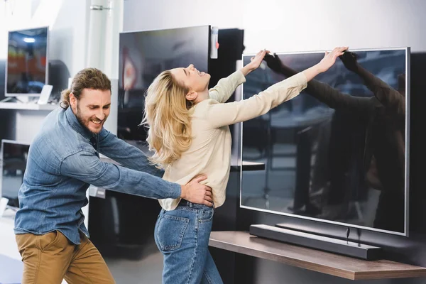Злой парень тянет подружку с телевизором в магазине бытовой техники — стоковое фото